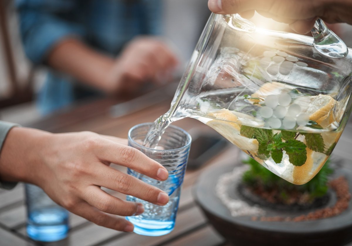 Person pouring water into a glass outside around a table